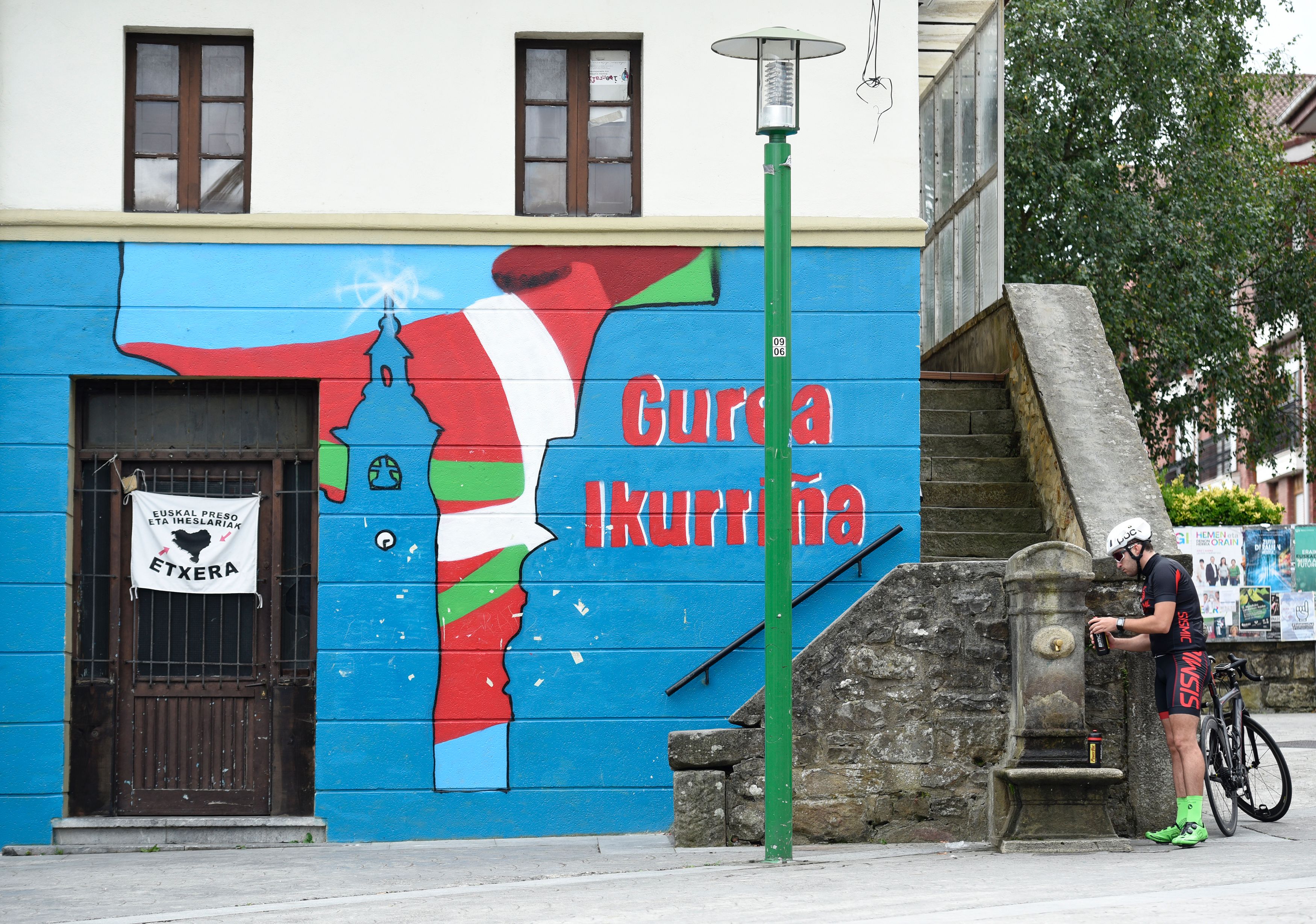 A cyclist fills a bottle with water of a fountain next to a mural painting reading in Basque "Ours, is Ikurrina" (Basque Country flag) in the main square of the Spanish Basque village of Larrabetzu during the Basque regional elections day on September 25, 2016. Spain's Basque country and Galicia went to the polls today in regional elections that may help unblock the long-lasting national political paralysis. / AFP / ANDER GILLENEA (Photo credit should read ANDER GILLENEA/AFP/Getty Images)